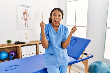 Ağrı kesici kliniğindeki güzel İspanyol fizyoterapist kadın kollarını kaldırıp, gözlerini açarak başarının şaşkınlığını ve şaşkınlığını kutluyor. Kazanan konsept. 