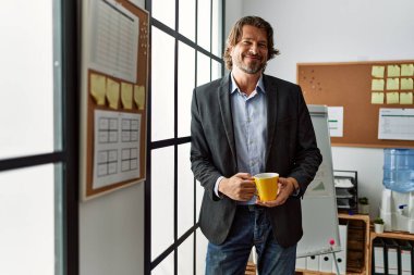 Orta yaşlı, beyaz, kendine güvenen, ofiste kahve içen bir adam.