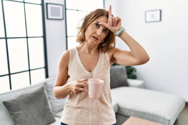 Orta yaşlı bir kadın evde kahve içiyor. Alnında parmakları olan insanlarla dalga geçiyor. Ezik jestler yapıyor.. 