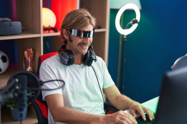 Oyun odasında sanal gerçeklik gözlüğü kullanarak video oyunu oynayan genç sarışın adam flaması.