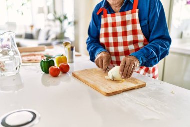 Kıdemli adam mutfakta soğan doğruyor.