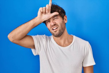 Latin kökenli genç adam mavi arka planda duruyor. Alnında parmakları olan insanlarla dalga geçiyor. Ezik hareketler yapıyor, alay ediyor, hakaret ediyor.. 