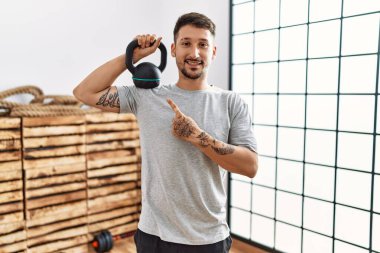 Spor kıyafetleri giyen genç yakışıklı adam halterlerle gülümsüyor mutlu bir şekilde el ve parmak gösteriyor. 