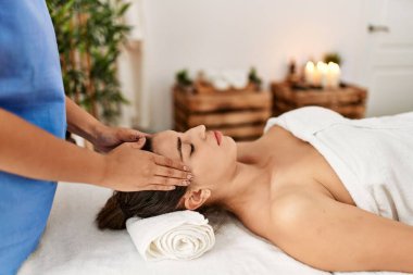 İki kadın terapist ve hasta güzellik merkezinde yüz masajı yapıyorlar.