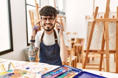 Sanat stüdyosundaki sakallı İspanyol adam yüksek sesli müzik için kulaklarını parmaklarıyla kapatıyor. sağır kavramı. 