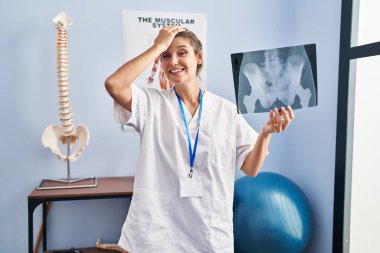 Elinde leğen kemiği radyografisi tutan genç bir kadın. Elleri başının üstünde, şaşırmış ve sinirli bir yüz ifadesi var. 