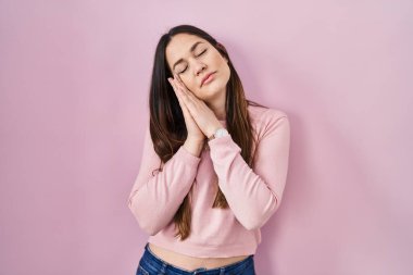 Genç esmer kadın pembe arka planda ayakta uyur. Yorgun düşler kurar, elleriyle poz verir ve gözleri kapalı gülümserdi.. 