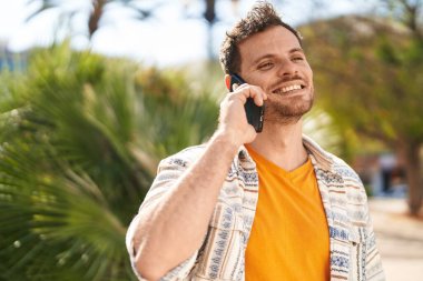Genç İspanyol adam gülümsüyor. Parktaki akıllı telefondan konuşuyor.