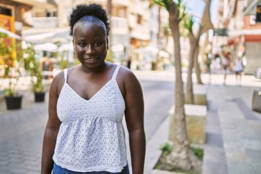 Genç Afrikalı Amerikalı kadın gülümseyerek şehirde mutlu mesut duruyor..