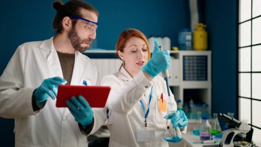 Laboratuvarda dokunmatik ped kullanan bilim adamı ve kadın üniforması giyiyor.