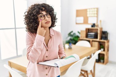 Ofiste iş elbisesi giymiş genç bir ortadoğulu kadın senin jestini ve şüpheli ifadeni izliyor. 