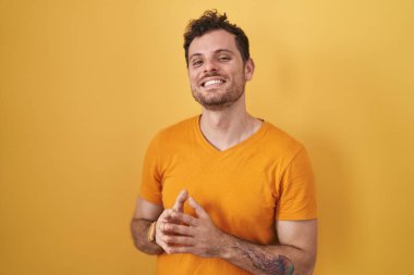 Sarı arka planda dikilen genç İspanyol adam el ele tutuşup gülümseyerek gevşemiş ve neşeliydi. Başarı ve iyimserlik 