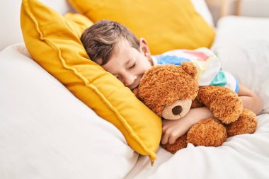 Sarışın çocuk oyuncak ayıyı kucaklıyor yatak odasında uyuyor.