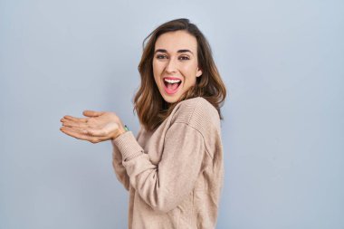 Young woman standing over isolated background pointing aside with hands open palms showing copy space, presenting advertisement smiling excited happy 