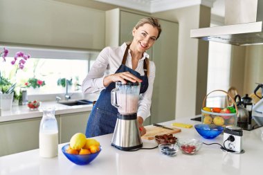 Genç sarışın kadın gülümsüyor. Kendine güveni tam. Smoothie 'yi sıvılaştırıyor.