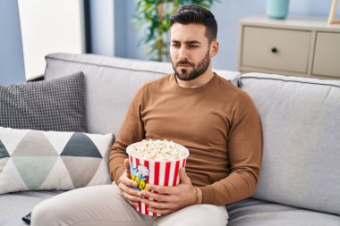 Evdeki kanepede oturup film izleyen sıkıcı İspanyol genç adam.
