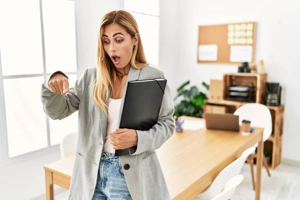 Blonde business woman at the office pointing down with fingers showing advertisement, surprised face and open mouth