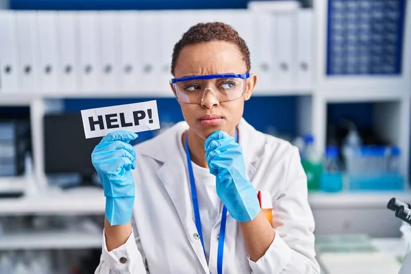 Beautiful african american woman working at scientist laboratory asking for help serious face thinking about question with hand on chin, thoughtful about confusing idea