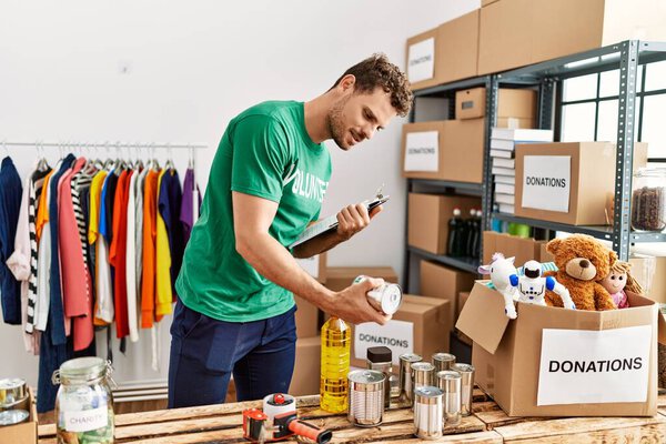 Молодой латиноамериканец в форме добровольца держит консервы в благотворительном центре