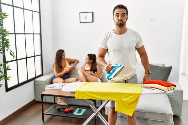 Joven Hombre Hispano Planchando Ropa Casa Soplando Mejillas Con Cara —  Fotos de Stock