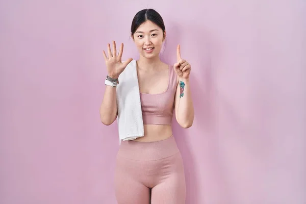 Chinese young woman wearing sportswear and towel showing and pointing up with fingers number six while smiling confident and happy.