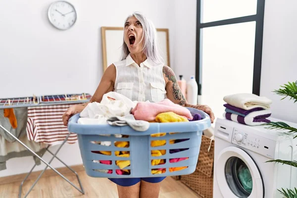 中年の白髪の女性を保持洗濯バスケット怒っていると怒っている叫び不満と激怒 怒りを見上げ叫びます — ストック写真