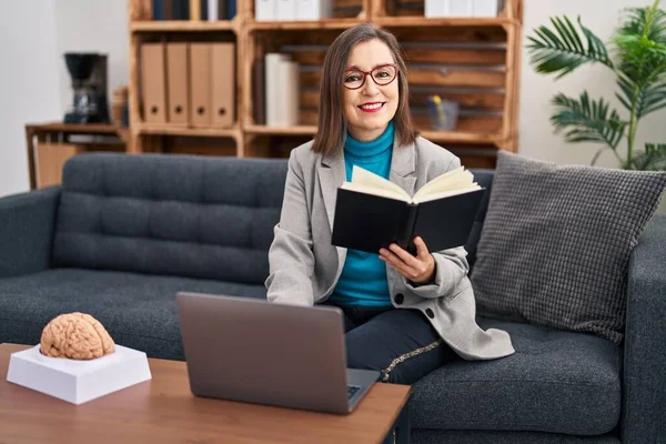 Middle age woman psychologist using laptop reading book at psychology center