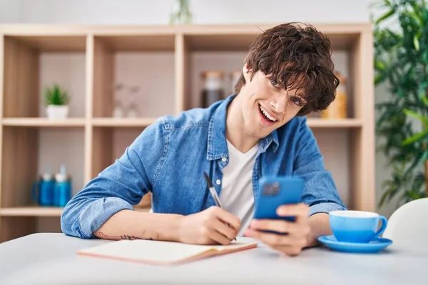 Young Hispanic Man Write Notebook Using Smartphone Home — Stock Photo, Image