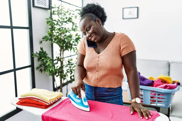 Молодая Африканская Американка Разговаривает Смартфону Гладит Одежду Дома — стоковое фото