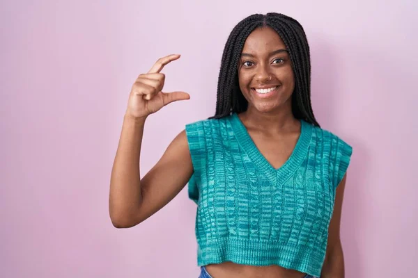若いアフリカ系アメリカ人は ピンクの背景の上に立っていて 指を見てカメラで小さなサイズのサインをして手で笑顔と自信を持ってジェスチャーをしています 概念を測定し — ストック写真