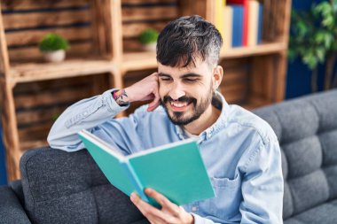 Evdeki kanepede oturmuş kitap okuyan genç bir İspanyol.