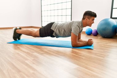 Genç İspanyol adam gülümsüyor spor merkezinde kendine güvenen karın kasları egzersizi yapıyor.