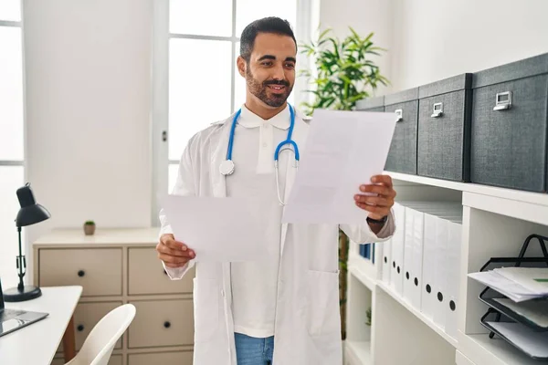 Young Hispanic Man Wearing Doctor Uniform Reading Report Document Clinic — Stock Photo, Image