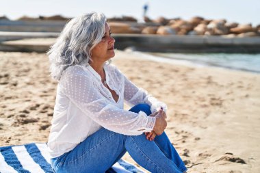 Middle age woman relaxed sitting on towel at seaside