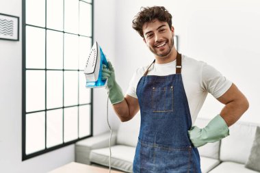 Genç İspanyol adam evde demir makinesini tutuyor.