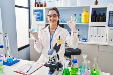 Laboratuvarda çalışan İspanyol kadın parmaklarıyla imza atıp gülümsüyor ve mükemmel bir sembol oluşturuyor. 