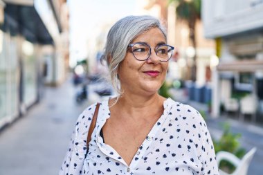 Orta yaşlı bir kadın sokakta kendine güvenerek gülümsüyor.