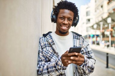 Afro saçlı, kulaklık takan ve akıllı telefon kullanarak müzik dinleyen yakışıklı bir zenci.