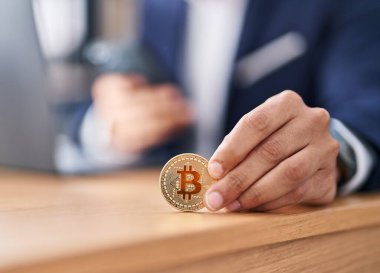 Genç İspanyol iş adamı ofisinde akıllı telefon kullanarak Bitcoin tutuyor.
