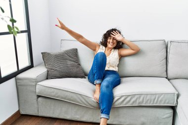 Orta Doğulu genç bir kadın, kendinden emin bir şekilde gülümsüyor evde müzik dinliyor.
