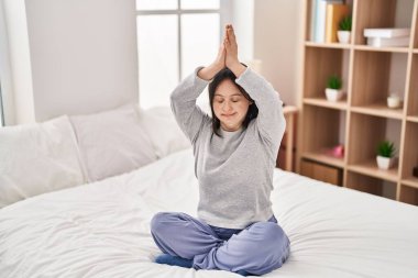 Down sendromlu genç bir kadın yatak odasında yoga egzersizi yapıyor.