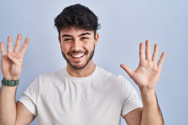Hispanic man with beard standing over white background showing and pointing up with fingers number nine while smiling confident and happy. 