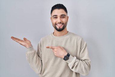 Soyutlanmış arka planda duran yakışıklı genç adam kameraya hayret içinde ve gülümserken eliyle ve parmağıyla işaret ediyor.. 