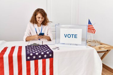 Genç Amerikalı siyasi parti çalışanı seçmen okulunda akıllı telefon kullanarak mutlu bir şekilde gülümsüyor..