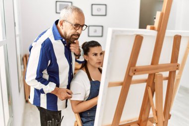 Resim öğretmeni, resim stüdyosunda tuvalde resim yapan genç bir kadına resim öğretiyor.