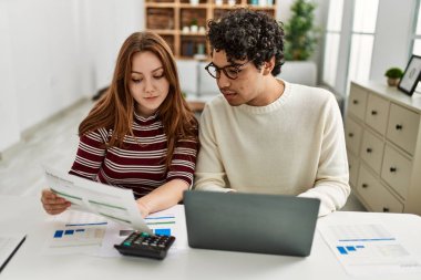 Ciddi ifadeleri olan genç bir çift evde masada dizüstü bilgisayar kullanıyor..