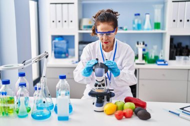Middle age hispanic woman looking through microscope at laboratory