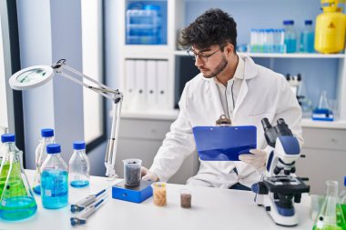 Young hispanic man scientist weighing sample reading document at laboratory