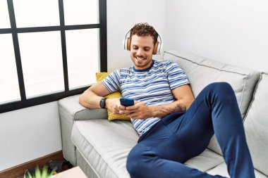 Genç İspanyol adam evde müzik dinlerken kendinden emin gülümsüyor.