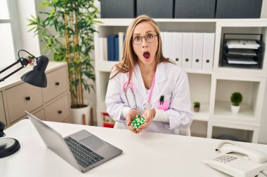 Sarışın kadın elinde şok edici bir yüz ifadesi olan haplar tutuyor. Şüpheci ve alaycı görünüyor. Ağzını açtığında şaşırıyor. 